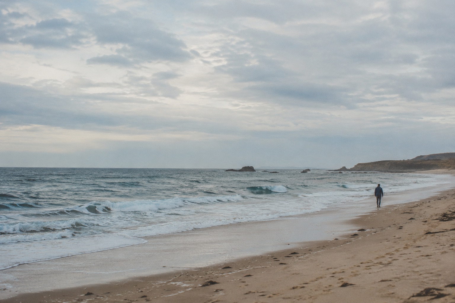 An imagined quiet coastline, with a small anonymous figure beside an expansive sea.